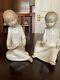 Two Nao (Lladro) figures both seated, girl reading a book and boy holding a ca